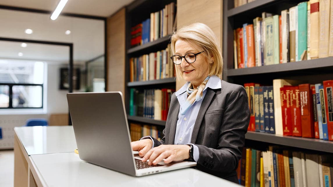 Female staff working on a laptop in a university library.