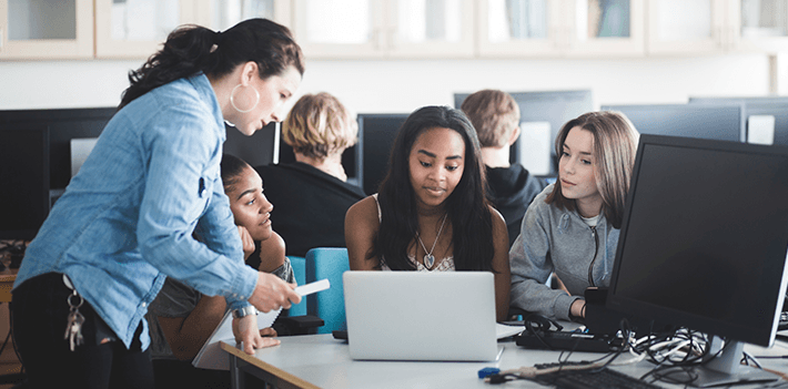 Colleague students receive help with their work from a teacher in a computer lab.