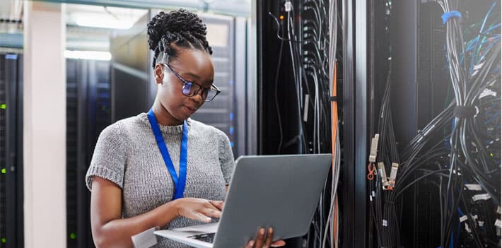 An IT worker looks at a laptop in a control room.