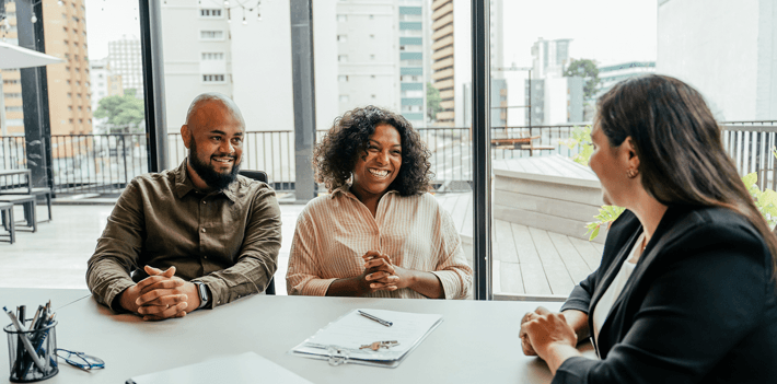 Three individuals are seated at a table in an office setting.