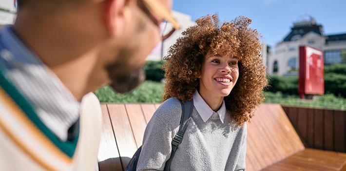 A teacher listens to an international student on a campus bench in the sunshine.